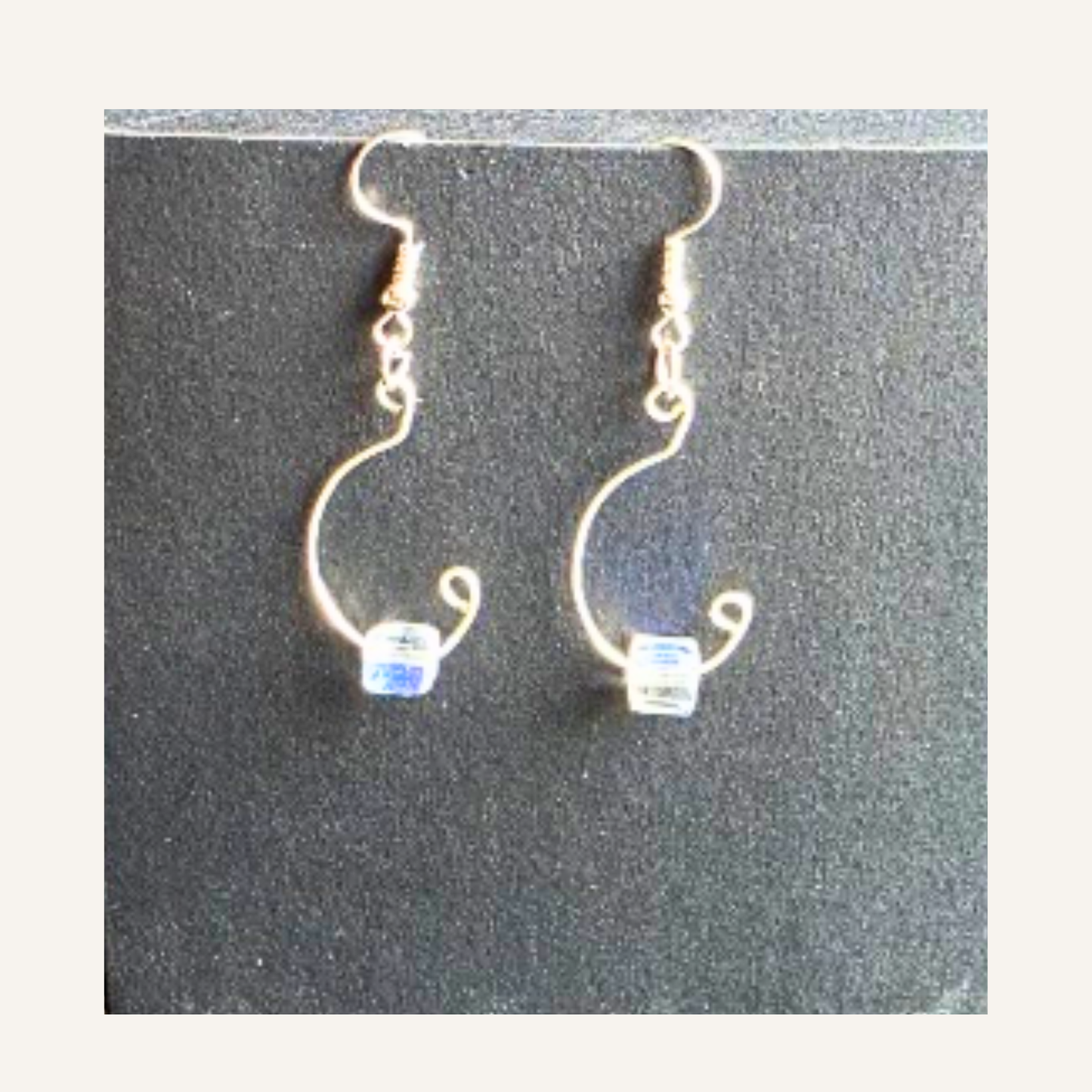 A pair of handmade wire hoop earrings with small clear faceted beads at the bottom, displayed on a dark textured background.