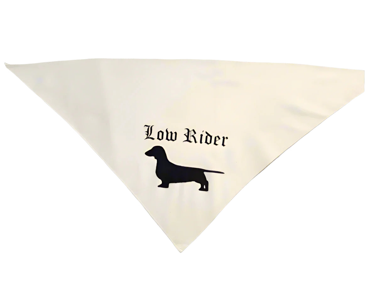 A white triangular pet bandana with a black silhouette of a wiener dog and the text 'Low Rider' printed on it.