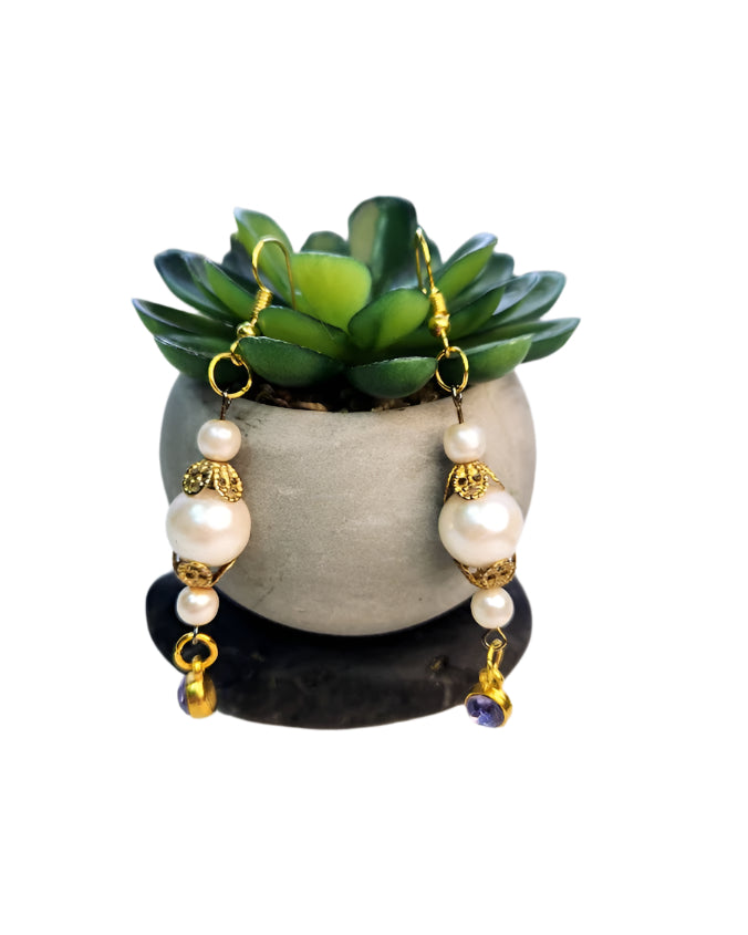 Handmade earrings with vintage faux pearls and purple crystals displayed in front of a potted plant.
