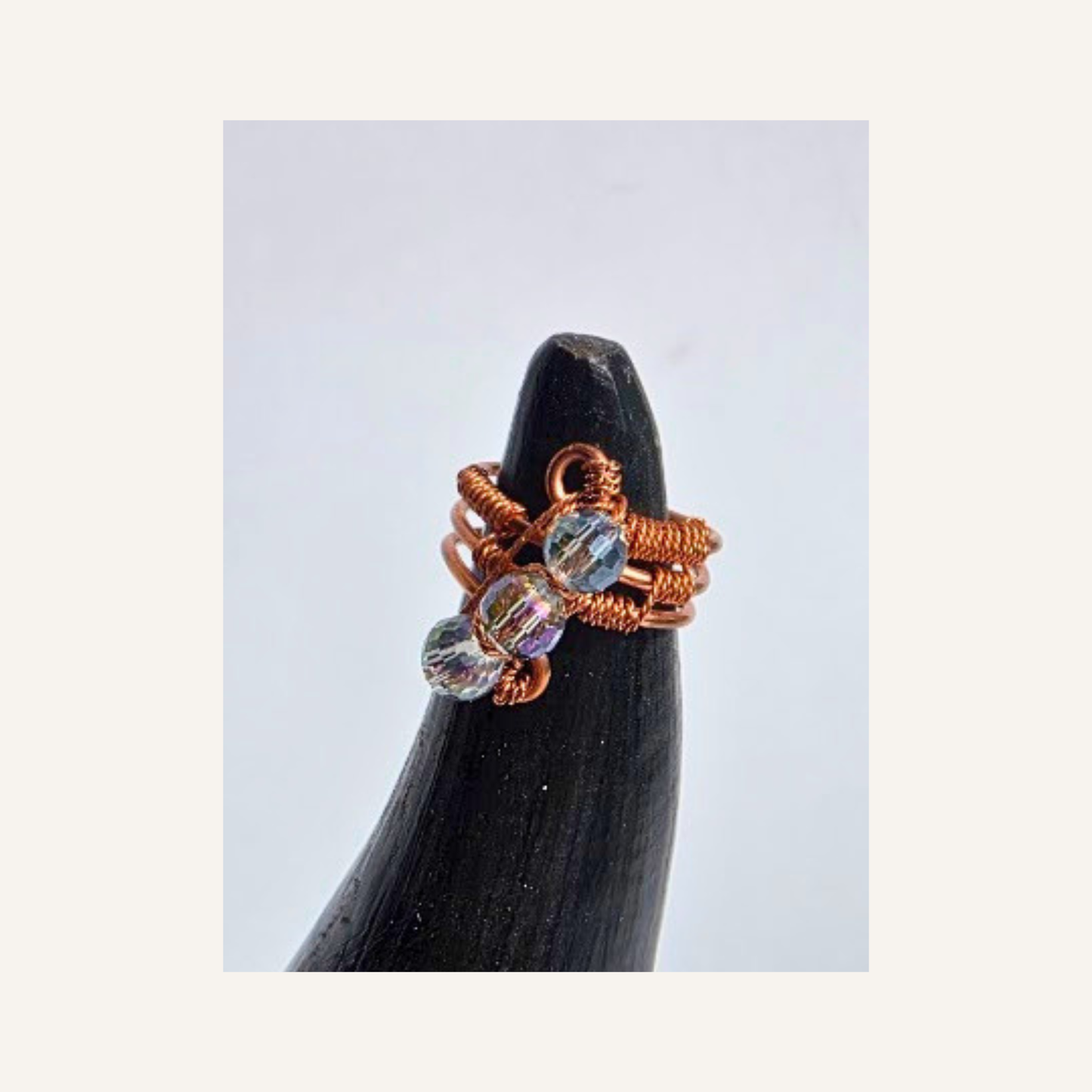 A handmade copper wire ring with three clear faceted beads, displayed on a black cone stand against a light gray background.
