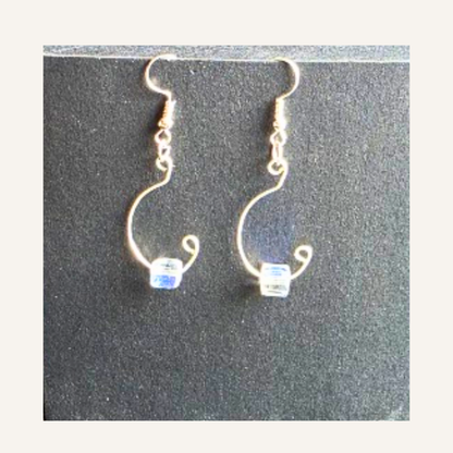 A pair of handmade wire hoop earrings with small clear faceted beads at the bottom, displayed on a dark textured background.