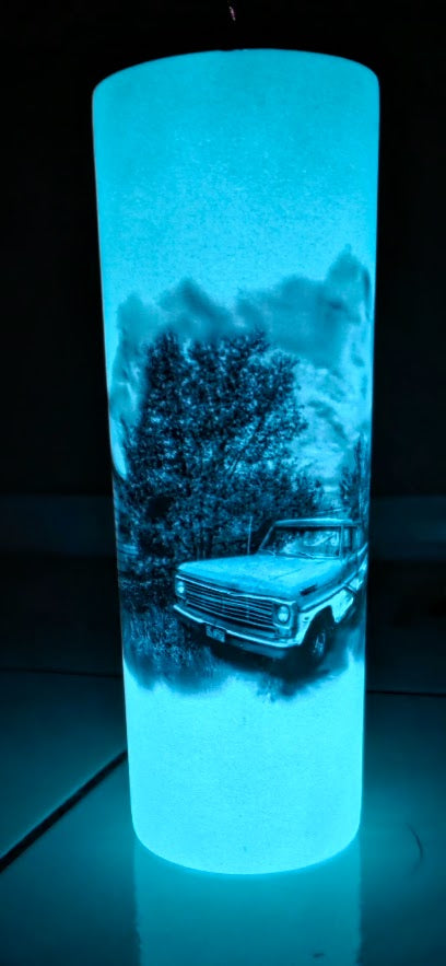 20 oz tumbler glowing with a bright cyan-blue light, featuring a printed black-and-white scenic graphic of a vintage pickup truck in a snowy forest.