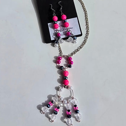A beaded necklace and matching drop earrings displayed on a black card. The jewelry features bright hot pink beads, clear faceted crystal beads, and small black beads on a silver-tone chain.