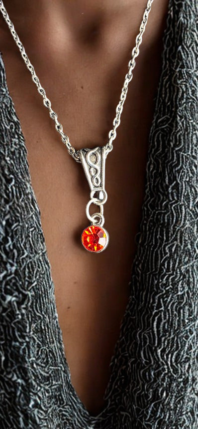 A close-up of a person wearing a silver chain necklace with a decorative silver bail and a round orange-red gemstone pendant, styled over a textured dark gray top.