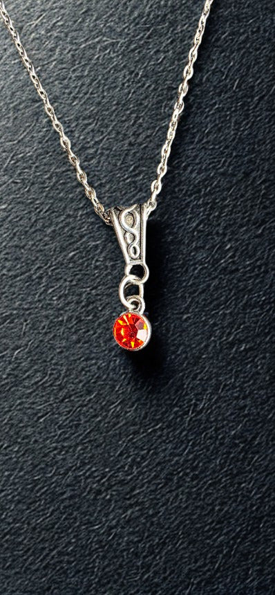 A silver chain necklace with a decorative silver bail and a dangling round orange-red gemstone pendant, shown on a dark textured background.