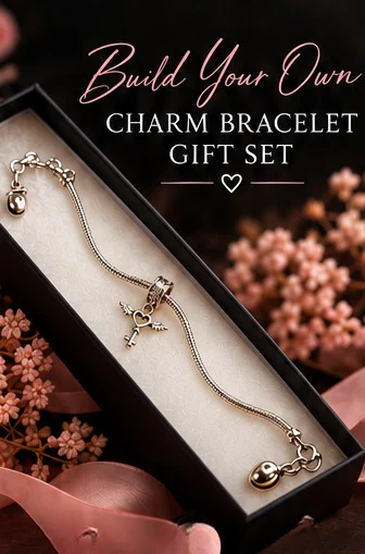 A silver charm bracelet displayed inside an open black gift box with a cream insert, surrounded by pink dried flowers and ribbon. Large text at the top reads 'Build Your Own CHARM BRACELET GIFT SET'.