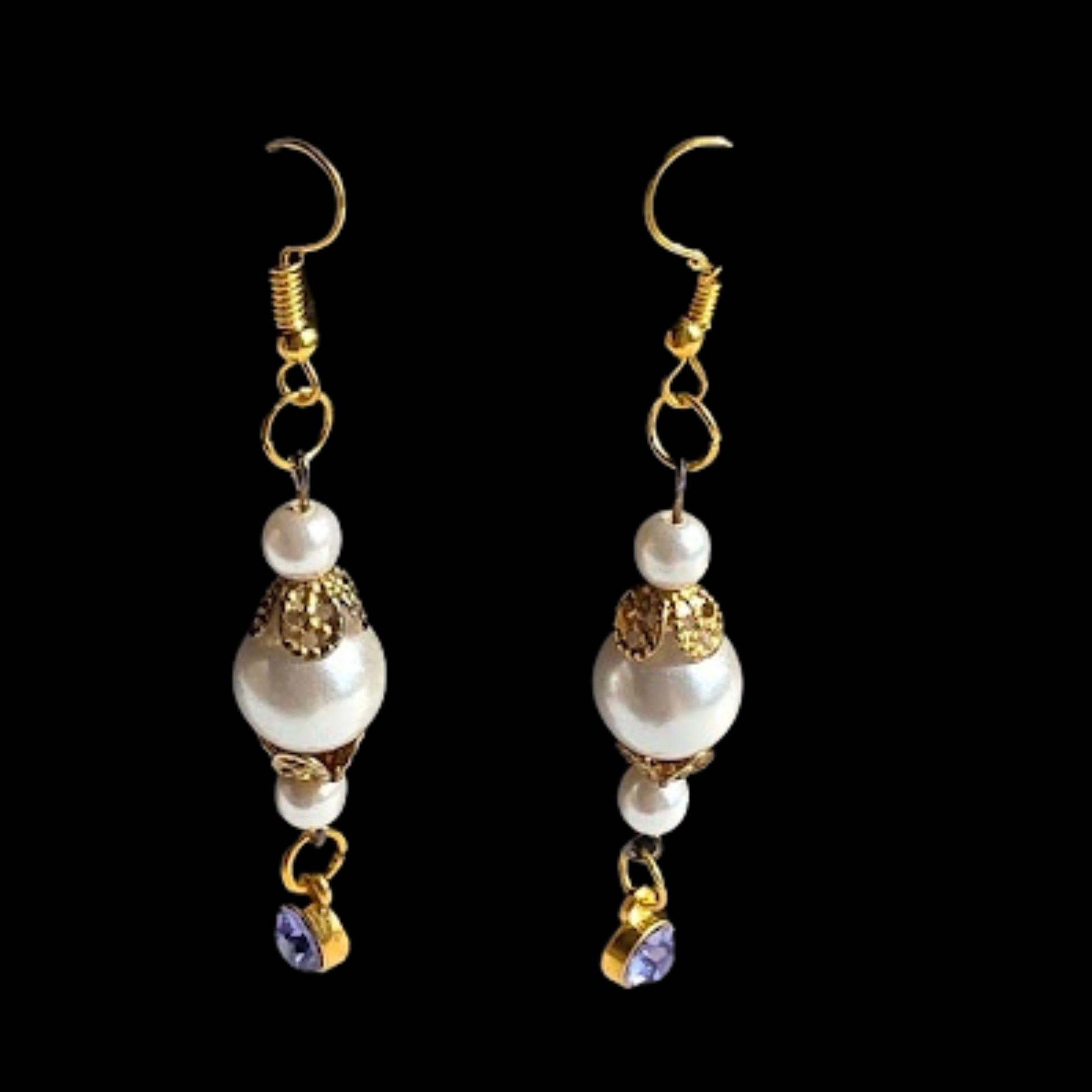A pair of gold and white drop earrings with white pearl-like beads, gold filigree details, and small purple crystal charms, shown against a solid black background.