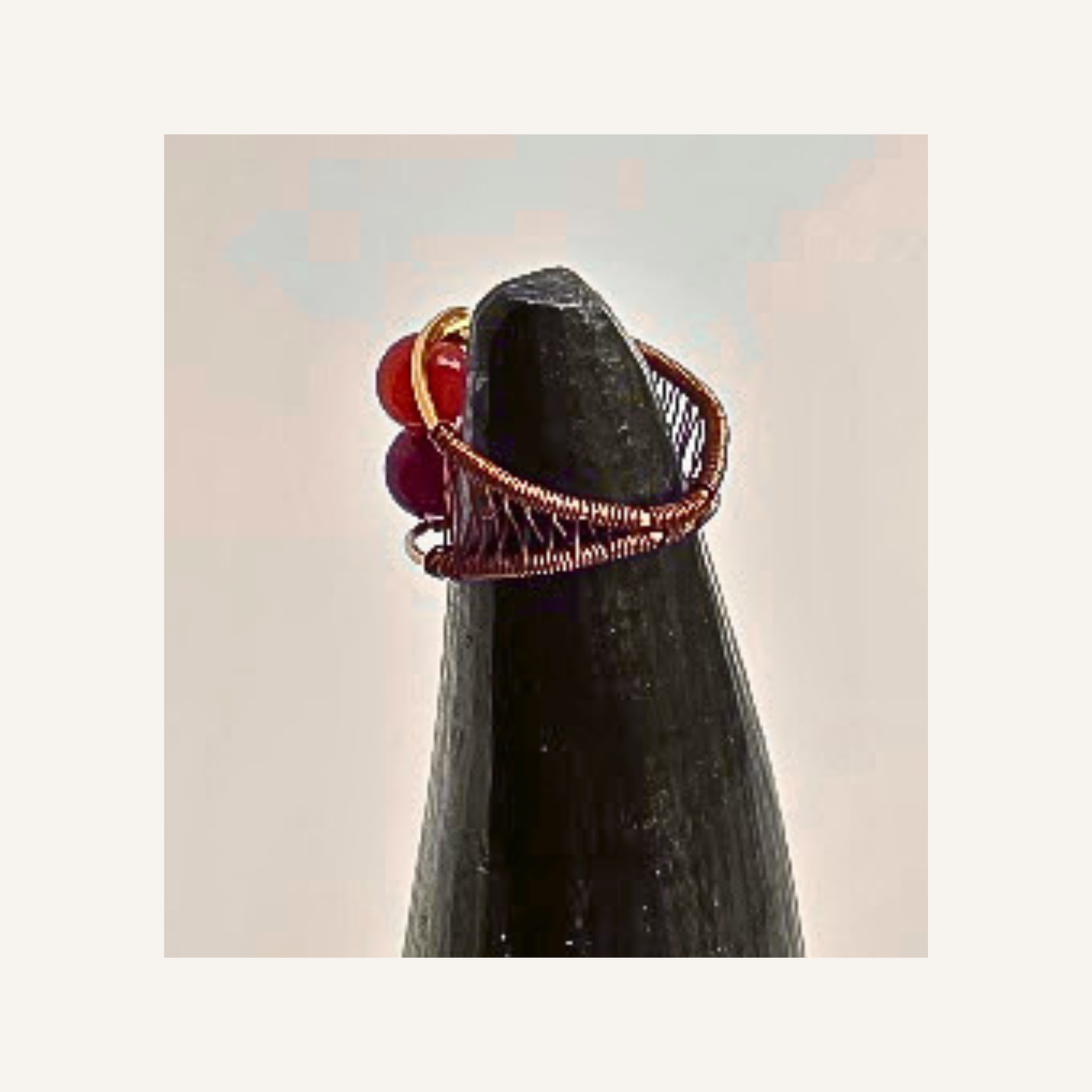 A handmade copper wire ring with red  agate gemstone accents, displayed on a black cone stand against a light beige background.