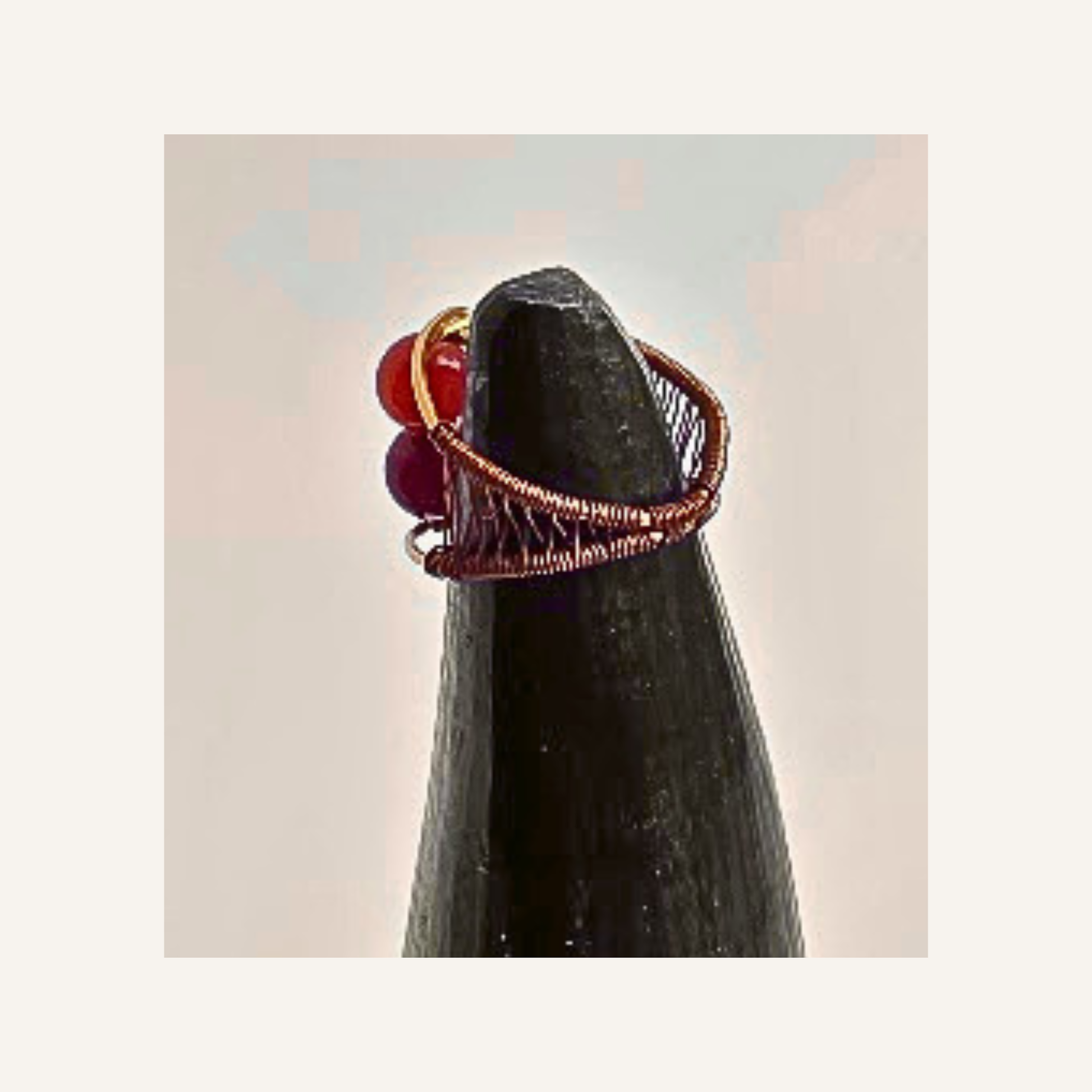 A handmade copper wire ring with red  agate gemstone accents, displayed on a black cone stand against a light beige background.