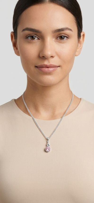 A woman wearing a delicate silver chain necklace with a round shaped pink gemstone pendant, shown against a neutral light gray background.