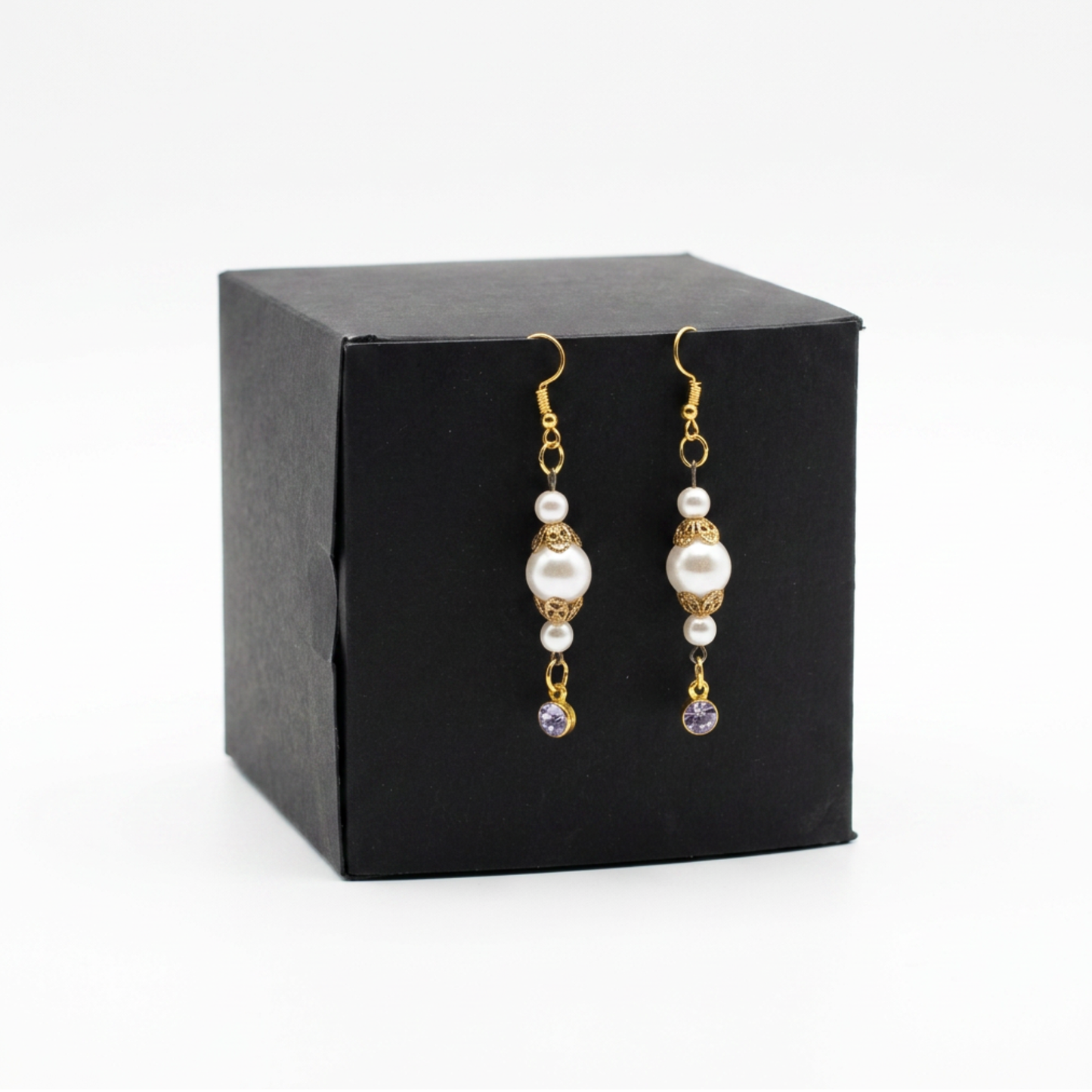 A pair of gold and pearl drop earrings displayed on a black square gift box against a white background.