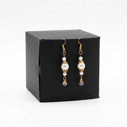 A pair of gold and pearl drop earrings displayed on a black square gift box against a white background.