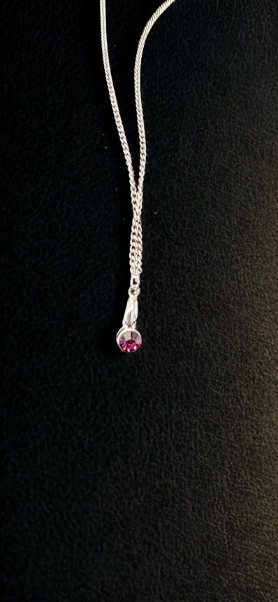 A silver-toned chain necklace with a teardrop-shaped pendant featuring a small round purple gemstone, displayed against a textured black background.