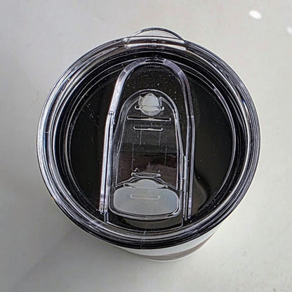 Top-down view of a clear plastic travel tumbler lid with a black rim and a transparent flip-up straw cover on a light gray surface.