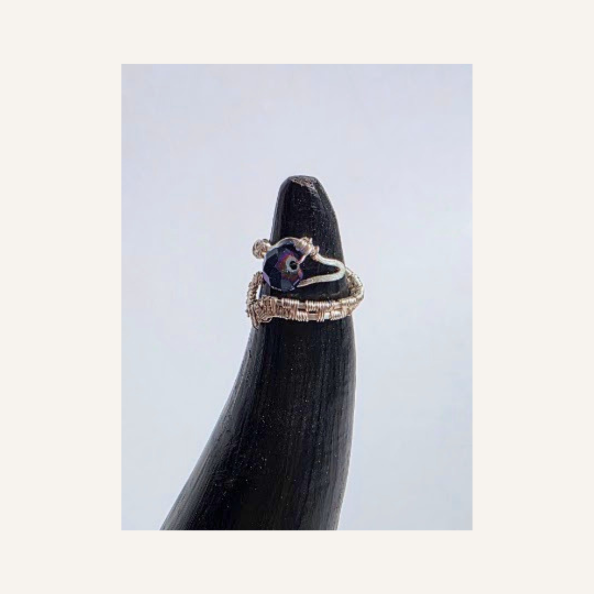 A silver ring with a dark iridescent purple-blue cabochon stone and small clear accent stones, displayed on a black ring stand against a light gray background.
