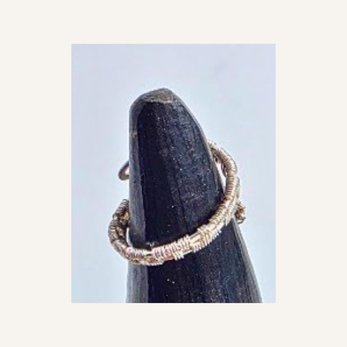A delicate silver wire ring wrapped around a dark display cone against a light gray background.