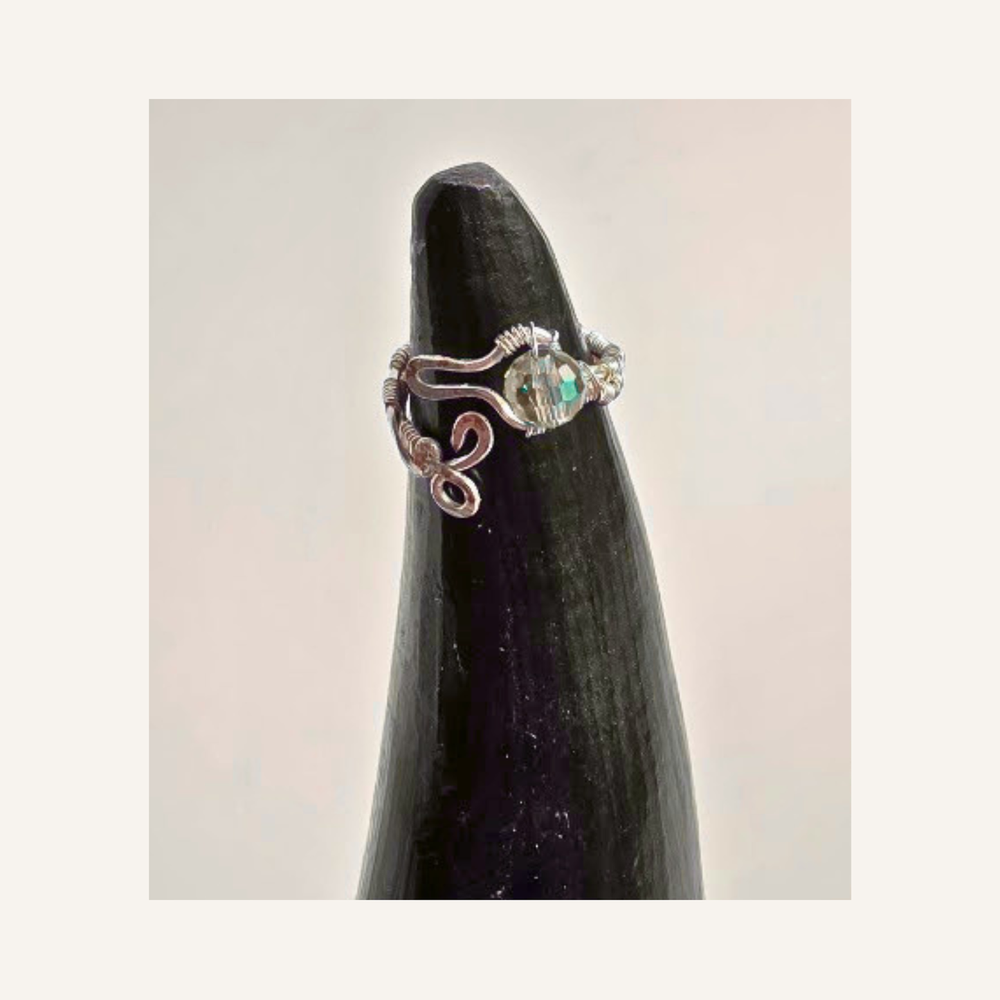 A silver ring with a iridescent  accent bead in light blue, displayed on a dark pointed stand against a light beige background.