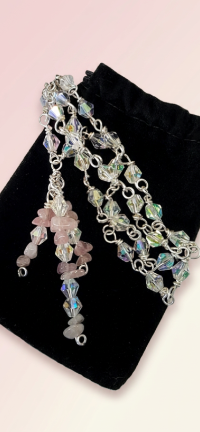 A silver-toned beaded necklace with iridescent and pink beads, displayed on a black velvet jewelry pouch against a pale pink background.