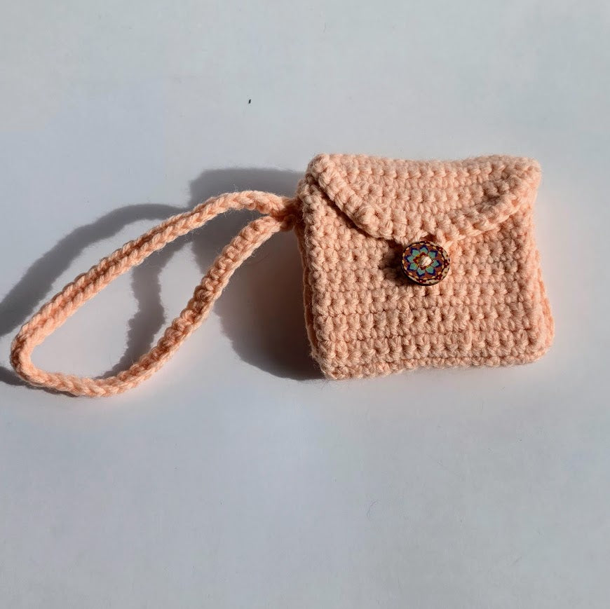 Shop a handmade peach crochet tri-fold wallet with wrist strap and button closure. Compact 4 x 4-inch handmade accessory crafted in Alberta, Canada. 