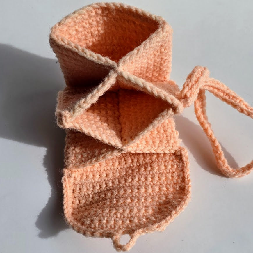 A handmade peach-colored crocheted pouch with a drawstring closure, photographed on a light gray background with a soft shadow.