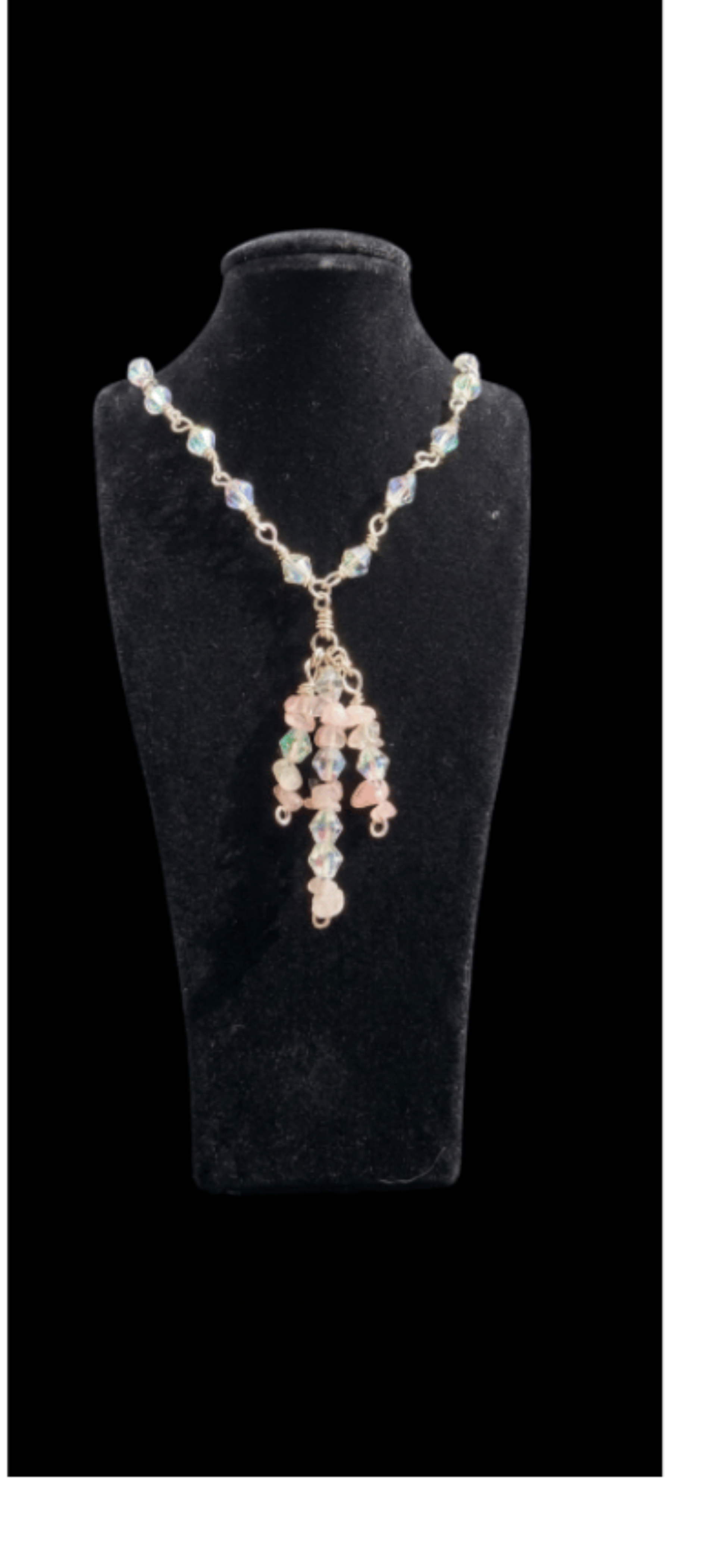 A gold-tone beaded necklace displayed on a black velvet jewelry bust against a black background. The necklace features a gold chain with clear faceted beads and a central drape of peach-pink, light blue, and green beads.