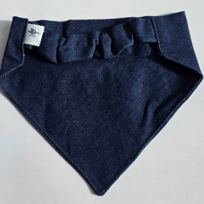A dark navy blue woven fabric pet bandana with a ruffled neck strap, laid flat on a light gray background. A small white brand tag is visible on the left side.