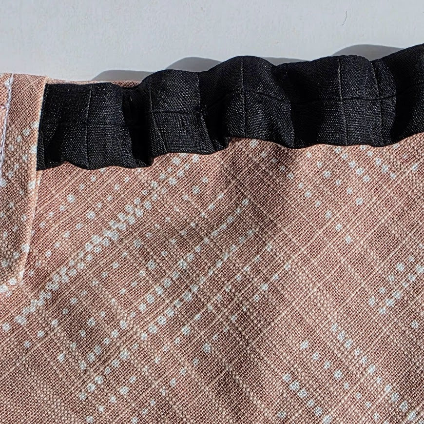 Close-up of a fabric product with a black pleated or gathered waistband and a dusty pink woven body featuring a white dotted grid pattern.