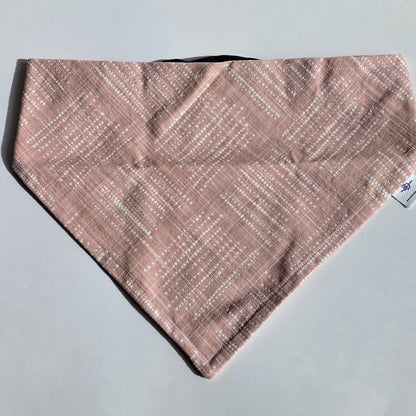 A triangular bandana-style pet bib or scarf in a dusty pink color with a white dotted diagonal pattern, laid flat on a light gray background.