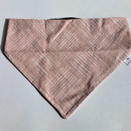 A triangular bandana-style pet bib or scarf in a dusty pink color with a white dotted diagonal pattern, laid flat on a light gray background.