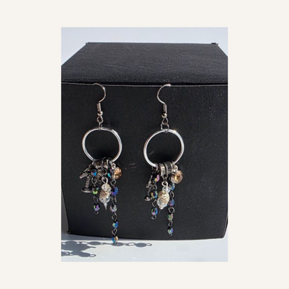 A pair of silver-toned dangle earrings with circular hoops and dangling charms, displayed against a black jewelry box on a light background.