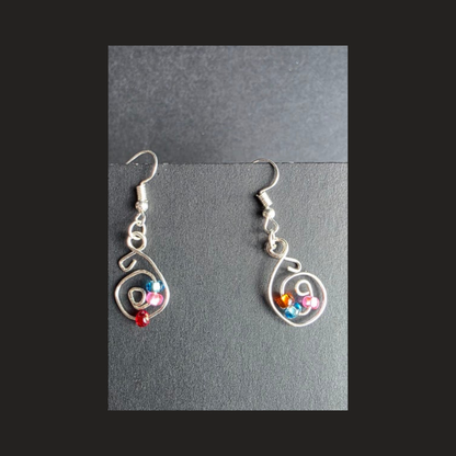 A pair of silver wire dangle earrings with small colorful beads, displayed on a dark gray textured surface.