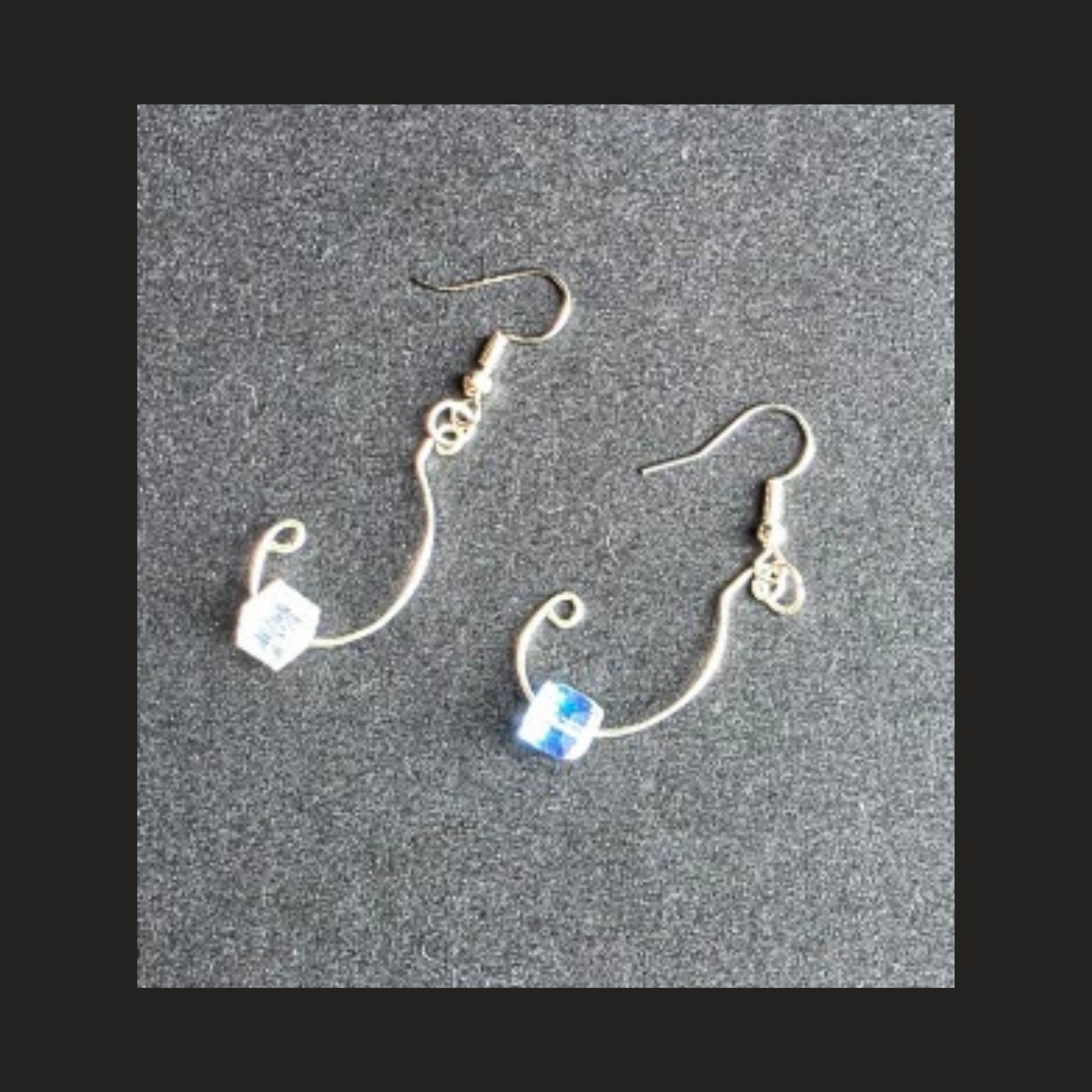 A pair of silver-plated dangle earrings with curved wire hooks, small decorative charms, and cube-shaped beads, displayed on a textured gray background.
Shop handmade silver-plated wire dangle earrings .
Lightweight handcrafted jewelry made in Alberta, Canada.