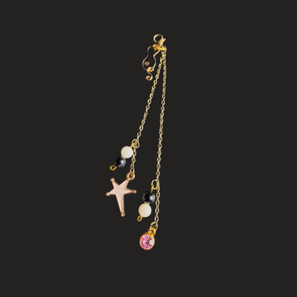 A gold-toned dangle earring with a starfish charm, white faux pearls, black beads, and a pink rhinestone charm, shown against a solid dark gray background.