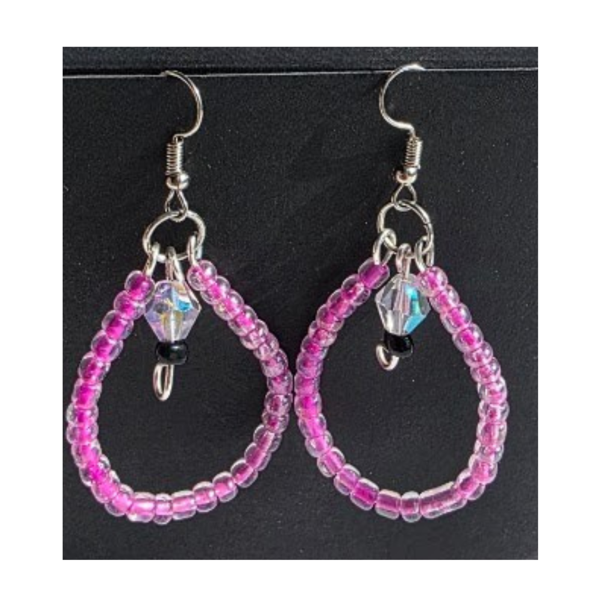 A pair of handmade beaded teardrop earrings with pink seed beads, silver-tone hooks, and iridescent faceted beads, displayed on a black background.