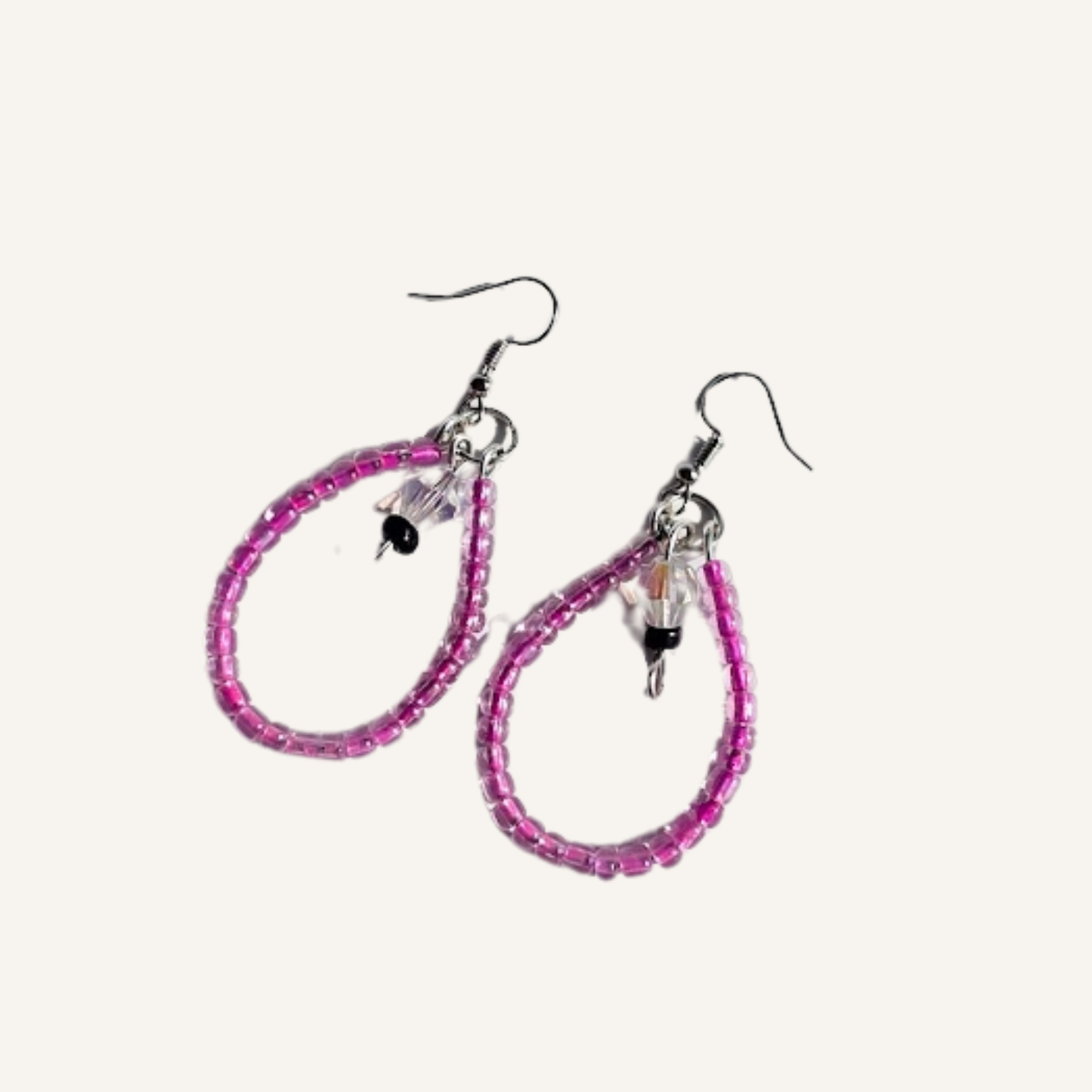 A pair of handmade teardrop hoop earrings made of pink faceted beads, featuring small dangling charms and silver fishhook ear wires, set against a plain off-white background.