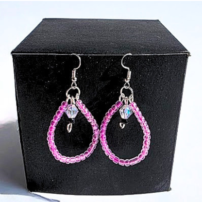 A pair of pink beaded teardrop dangle earrings with silver hooks and small faceted crystal charms, displayed on a black velvet jewelry box.