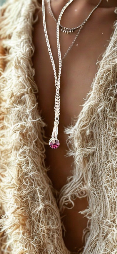 A close-up of a model wearing a silver lariat necklace with a purple gemstone pendant, layered over a beige fringed cardigan.