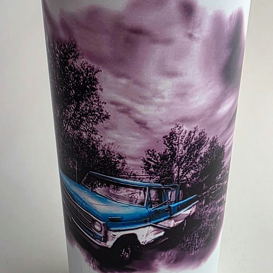 A white cylindrical tumbler featuring a printed graphic of a vintage blue pickup truck in a rural setting under a cloudy purple-toned sky.