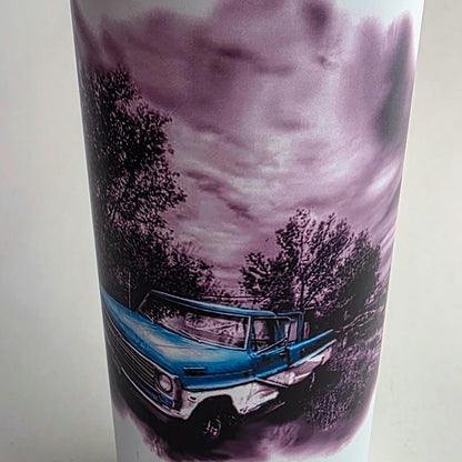 A white cylindrical tumbler featuring a printed graphic of a vintage blue pickup truck in a rural setting under a cloudy purple-toned sky.