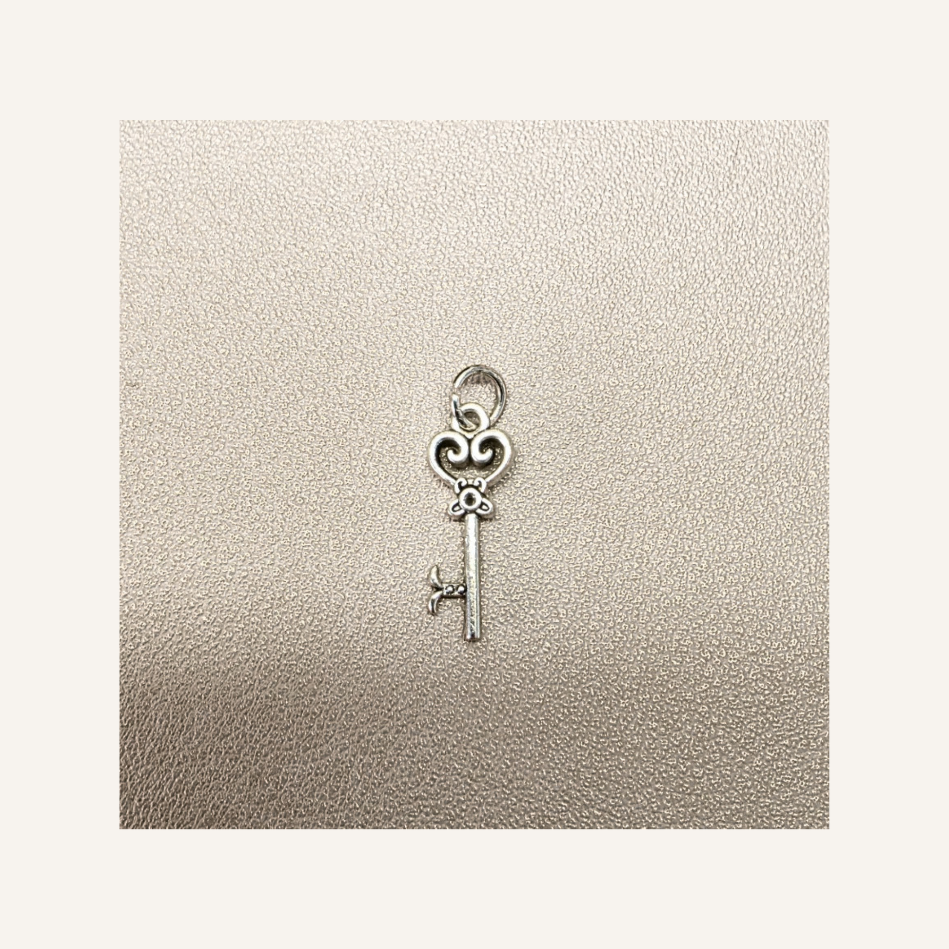 A small silver key-shaped charm with a heart-shaped top, displayed on a textured beige surface.